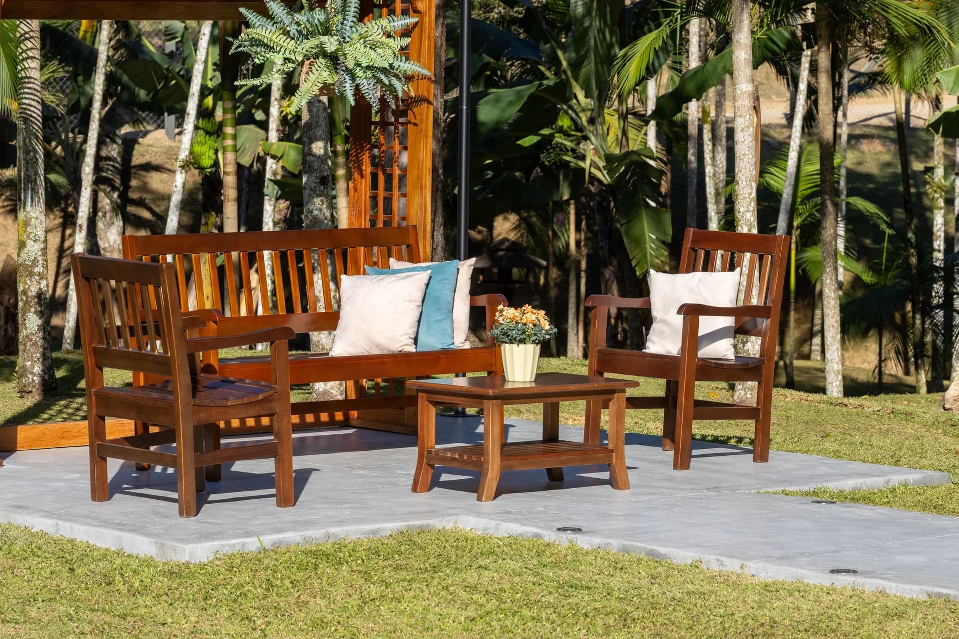 Sofá, sillones y mesa de centro de madera de Móveis Daniella en un jardín con palmeras